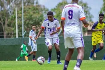 Jeune footballeur en maillot blanc et violet dribblant le ballon sur un terrain vert.