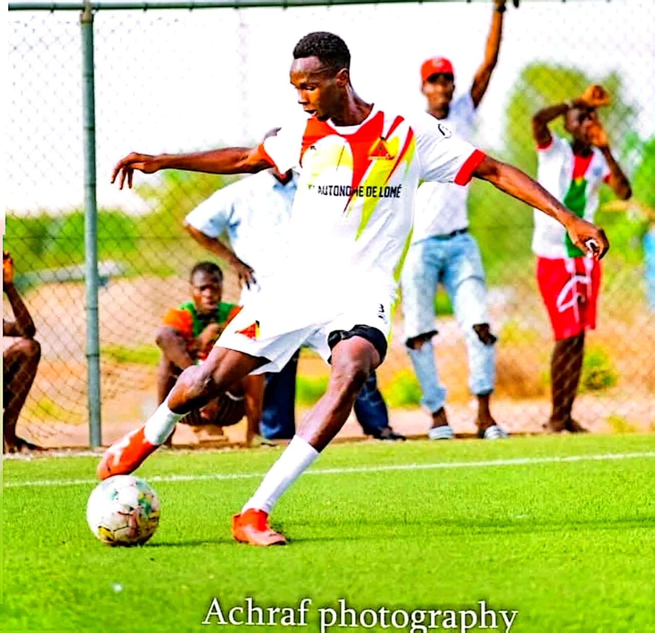 Un footballeur en maillot blanc et rouge frappe un ballon sur un terrain de sport.