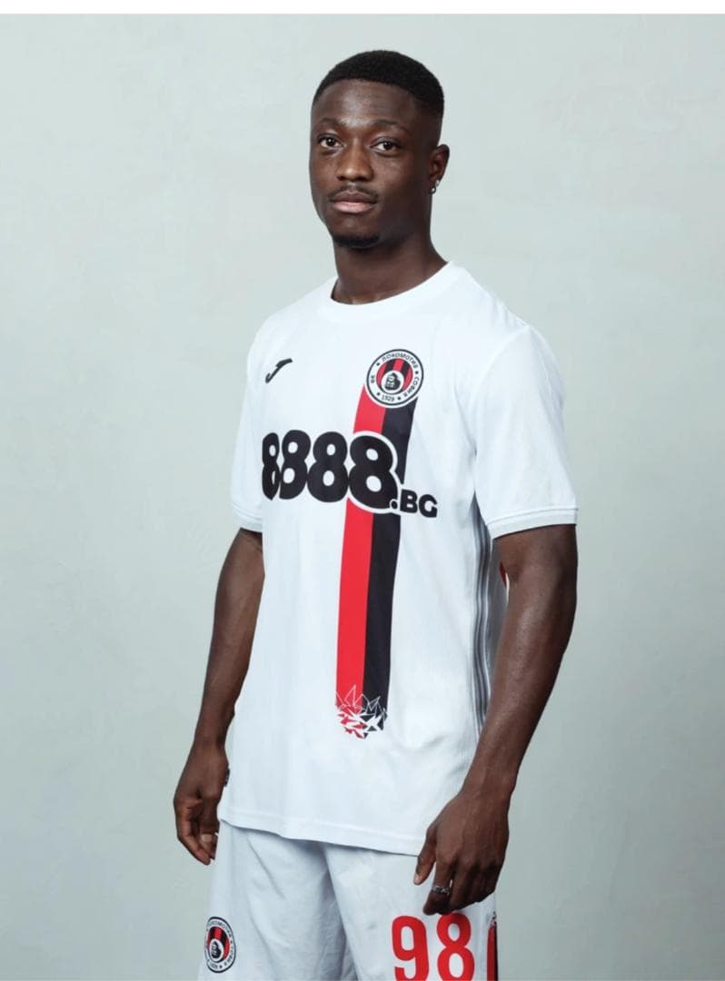 Un footballeur en maillot blanc avec une bande verticale rouge et noire sur fond gris.