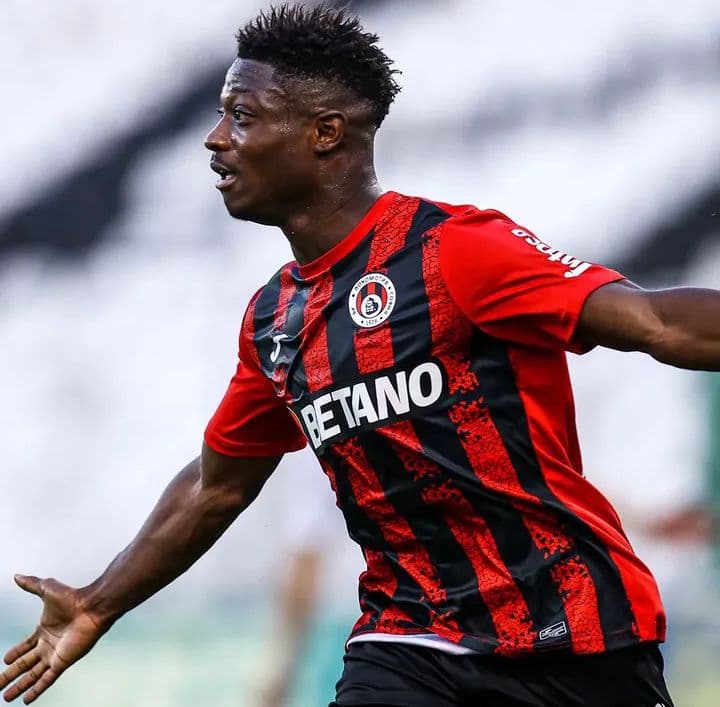 Footballeur noir en maillot rayé rouge et noir célébrant avec enthousiasme sur le terrain.