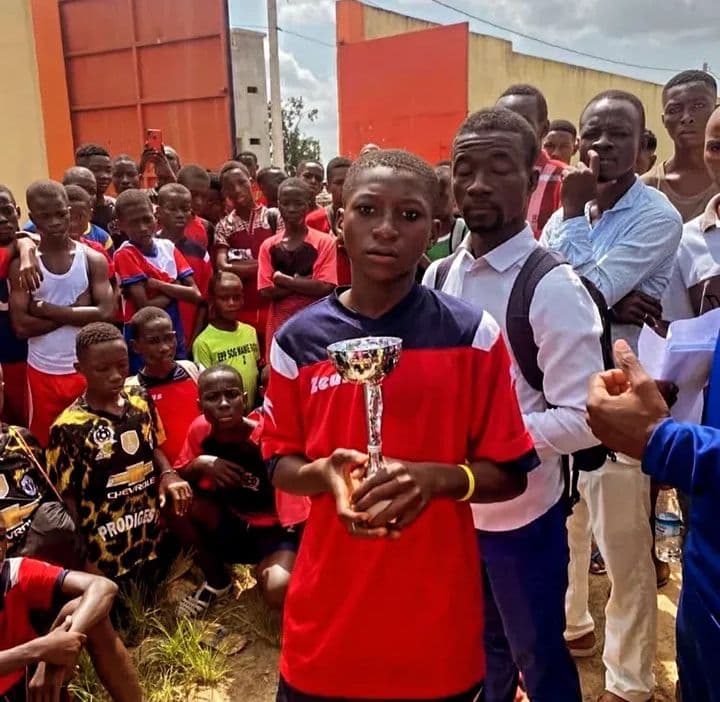 Un jeune garçon en maillot rouge tenant un trophée d'argent devant une foule de spectateurs.