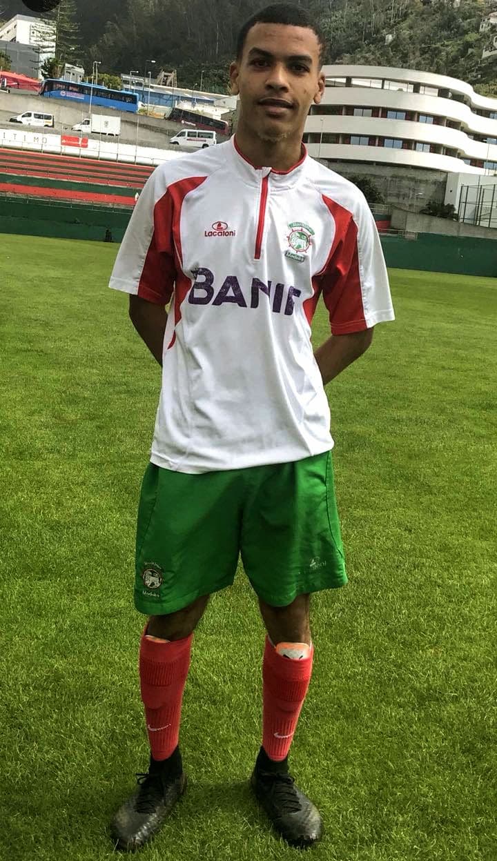 Jeune footballeur en tenue blanche et rouge debout sur un terrain de sport.