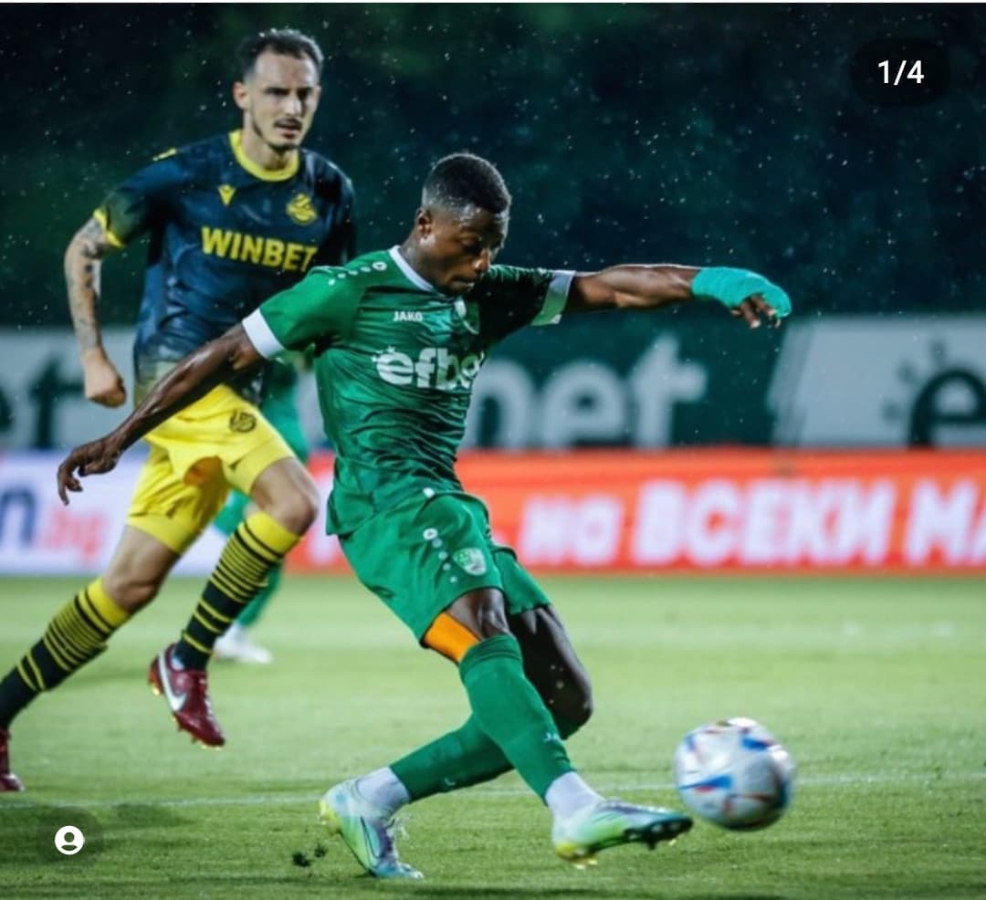 Un footballeur en maillot vert frappe le ballon devant un adversaire en jaune.